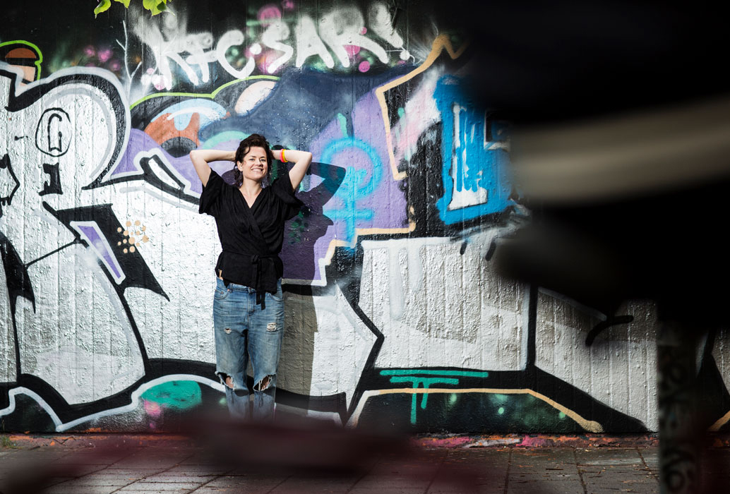 En kvinna poserar vid en graffitivägg