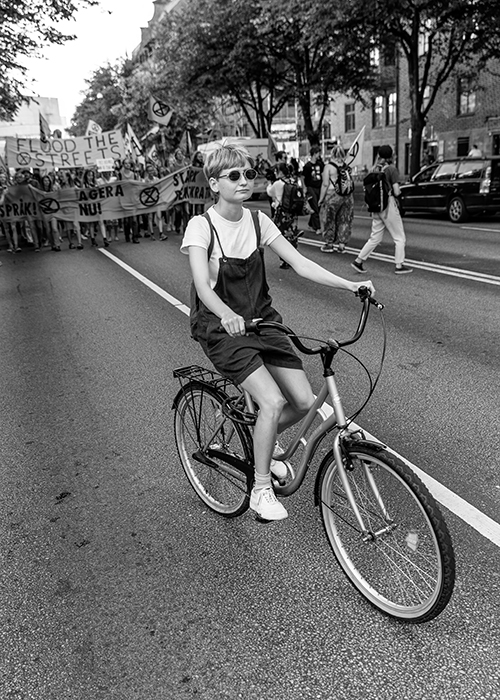 En kvinna på en cykel med demonstrationståg i bakgrunden