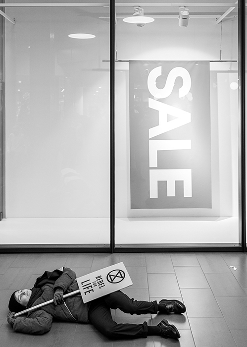 Ung person ligger ner med en aktivistskylt utanför ett skyltfönster