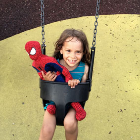 En flicka gungar med ett Spider Man gosedjur
