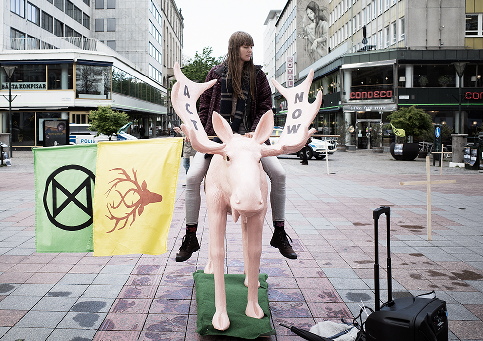 En ung kvinna sitter på en rosa älg skulptur i Malmö